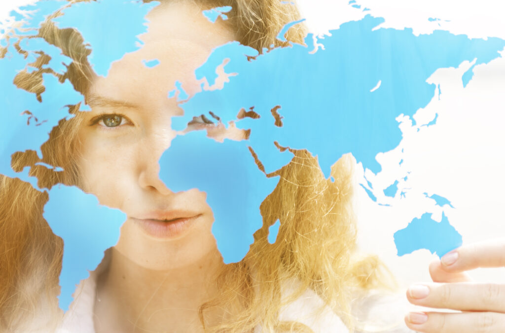 A blonde person peers at a vinyl cut-out of the world map suspended on a window