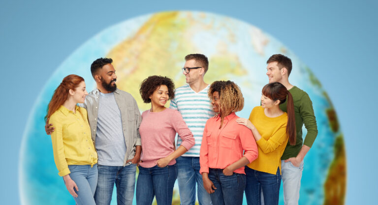 A multi-ethnic group stand against a backdrop of the planet earth, smiling at one another
