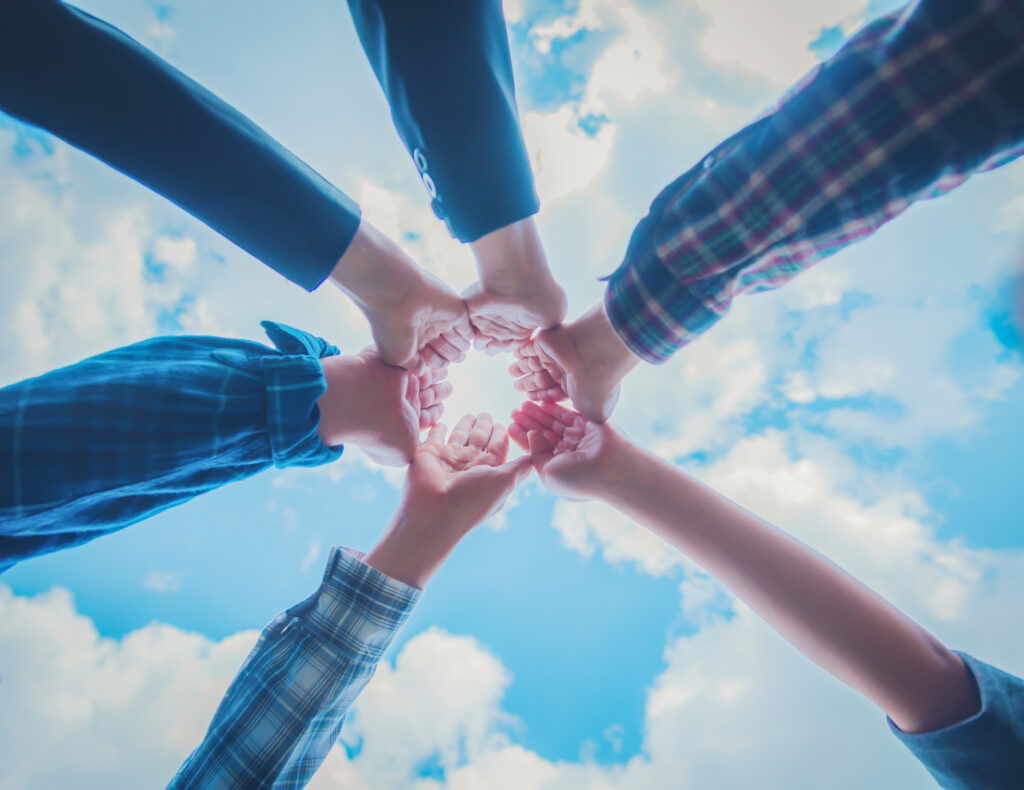 Six different arms put their hands in against the backdrop of a blue cloudy sky