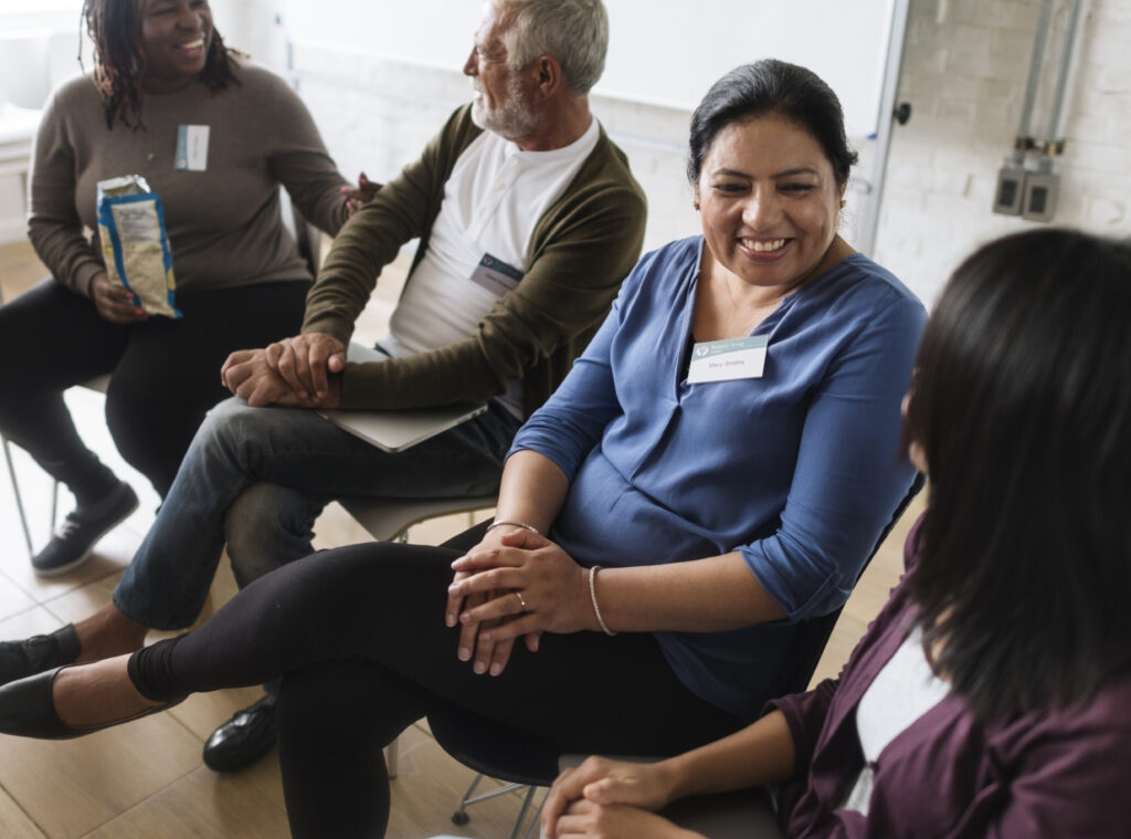 A group of four people sat on chairs in polite conversation, smiling